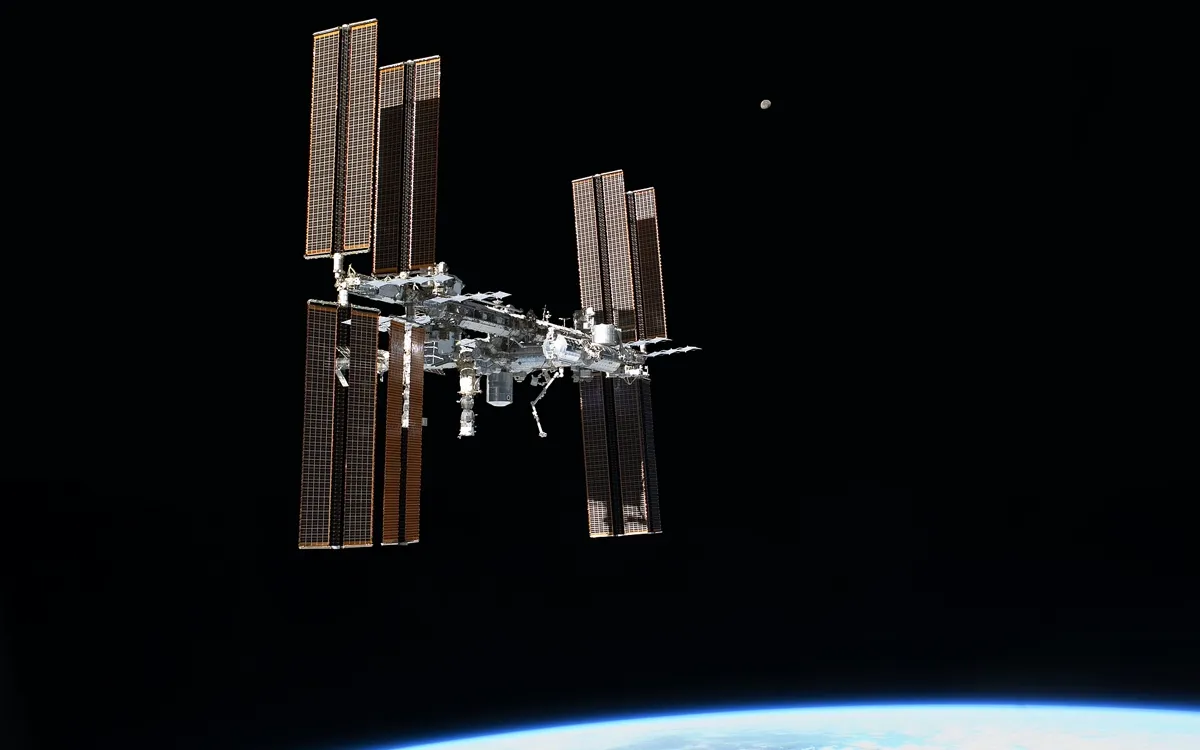 The International Space Station with its solar arrays extended, photographed against black space above Earth's horizon