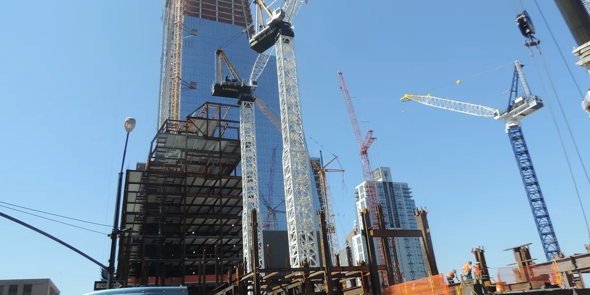 Tower cranes and a steel frame rising beside a glass skyscraper on a large Manhattan construction site